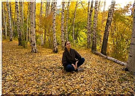 A woman sitting on the ground meditating in a forest. 